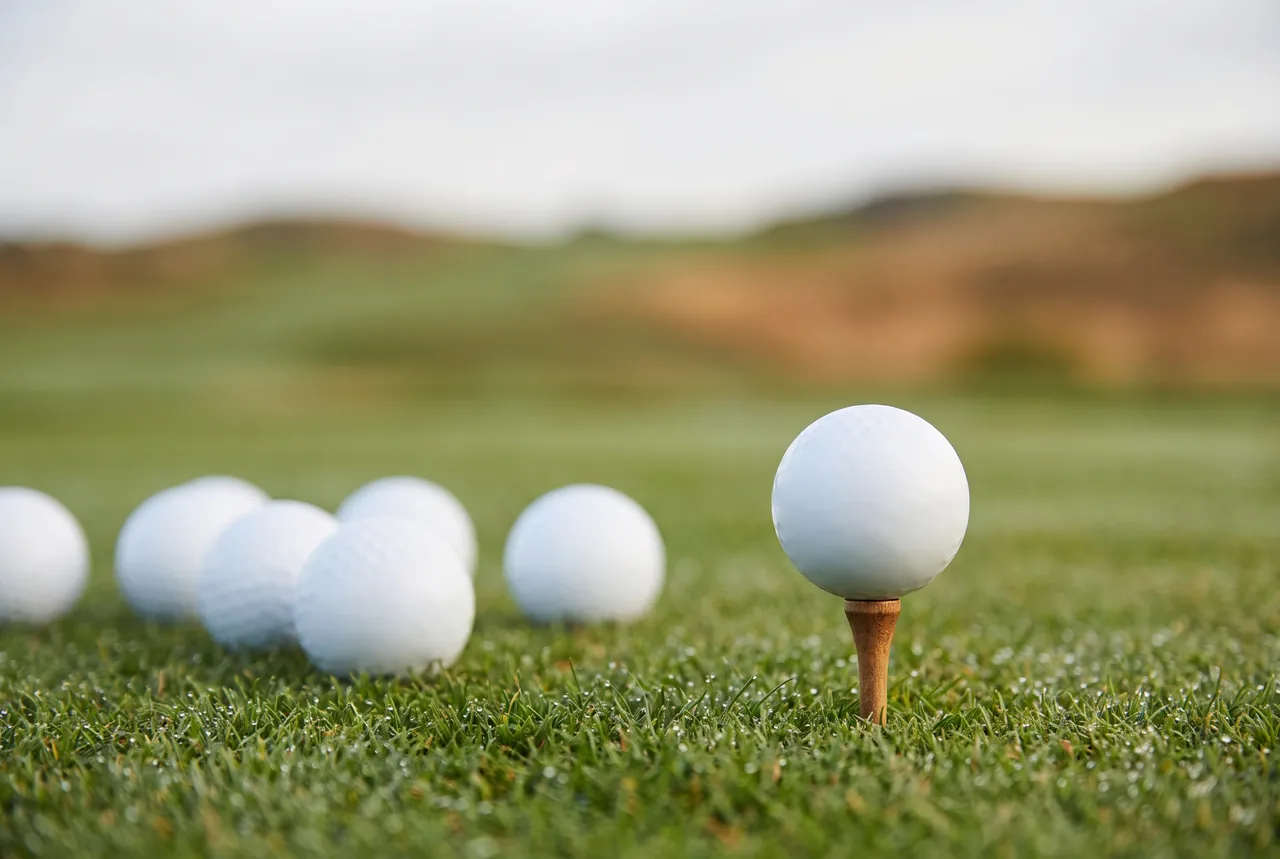 Plain white golf balls on dewy fairway grass with one golf ball on a wooden tee